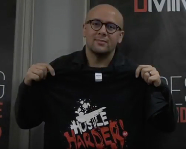 A man holding up his t-shirt with the words " hustle harder !" on it.