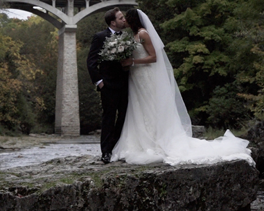 A bride and groom kissing on the side of a bridge.