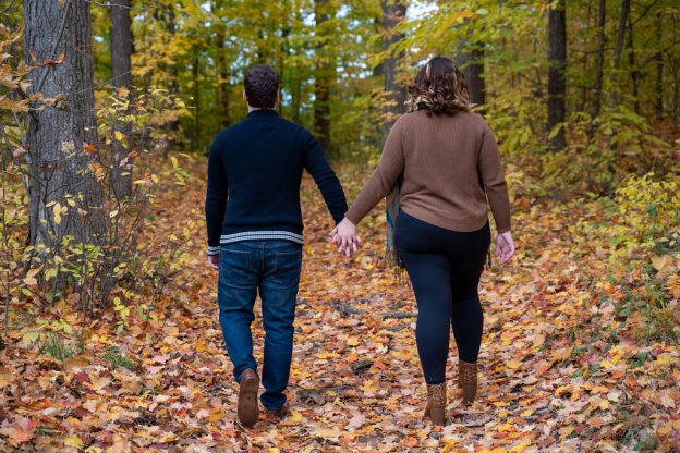 A man and woman holding hands while walking through the woods.