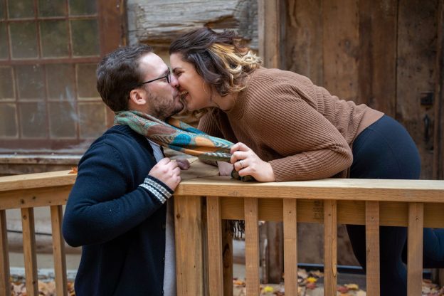 A man and woman kissing on the side of a wooden deck.