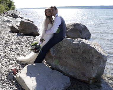 A newly married couple sitting on top of rocks near the water.