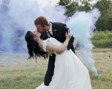 A bride and groom kissing in front of smoke.